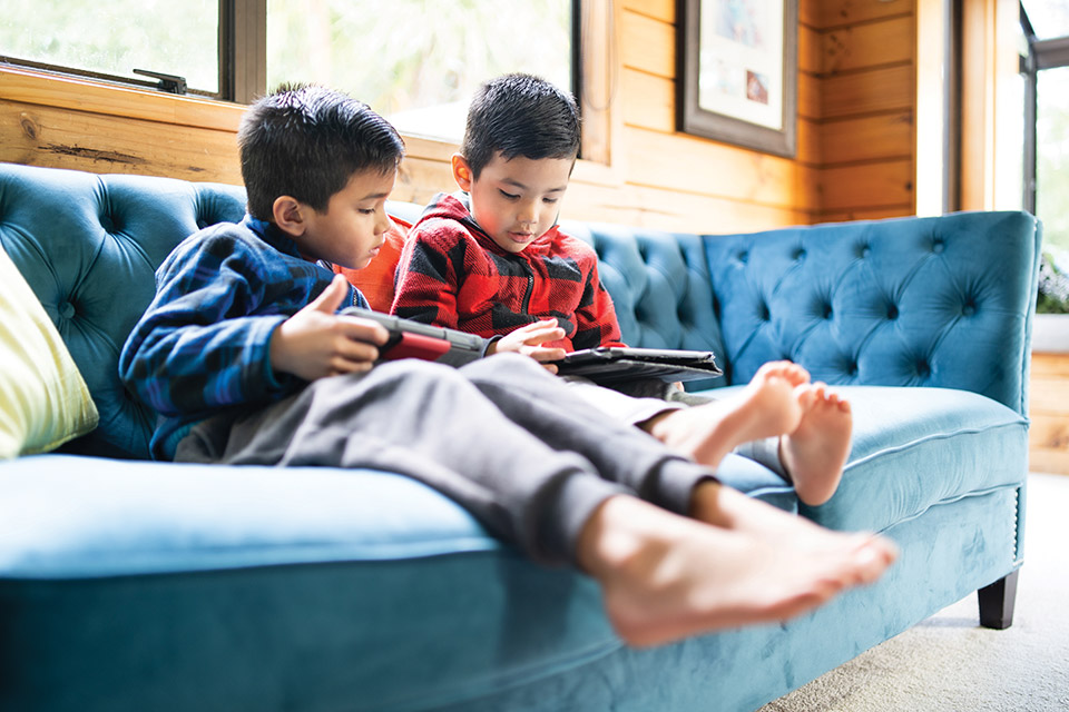 Children looking at iPads on a couch (photo by iStock)