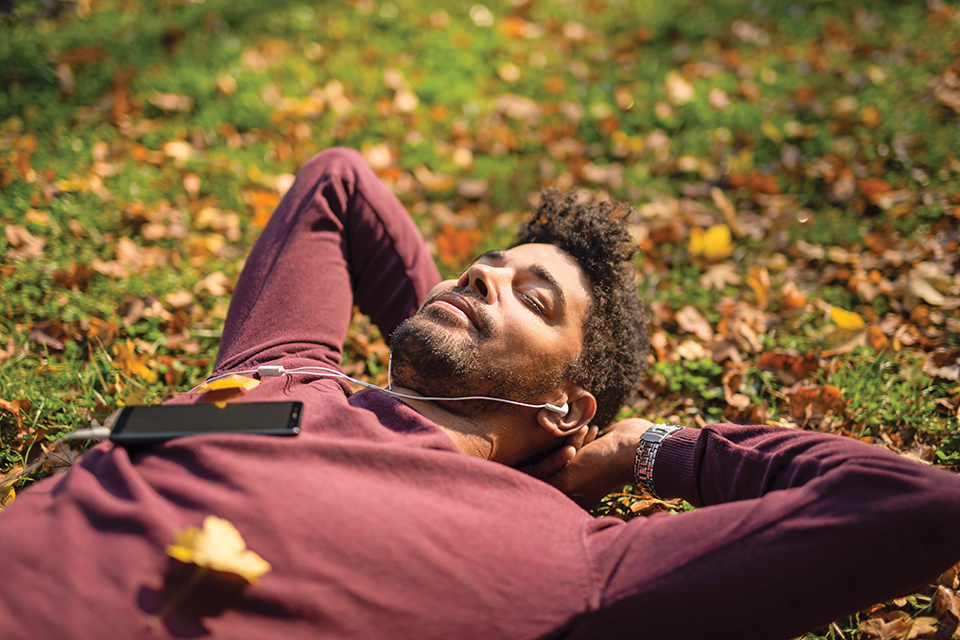 Man listening to mobile phone with headphones and laying in leaves (photo by iStock)