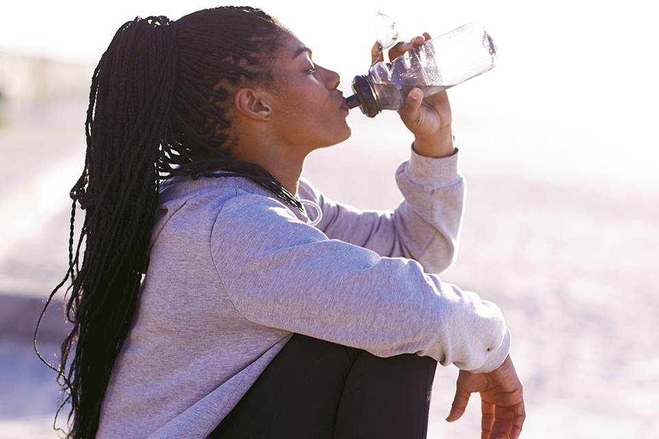 Woman drinking water out of reusable bottle (photo by iStock)