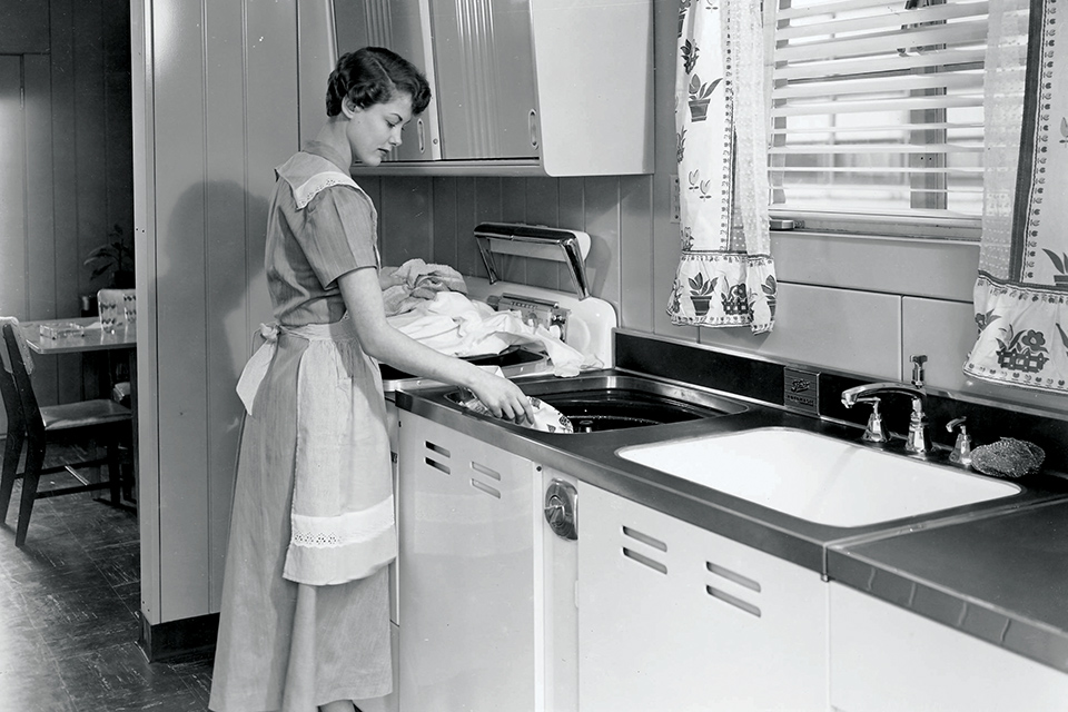 Woman using built-in washer of a Lustron home (photo courtesy of Ohio History Connection)