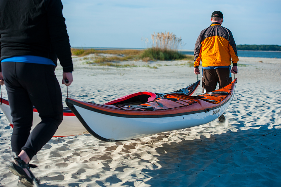 Men carrying 2 kayaks down the beach